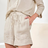Person wearing beige shorts and shirt with lace trim on a white background