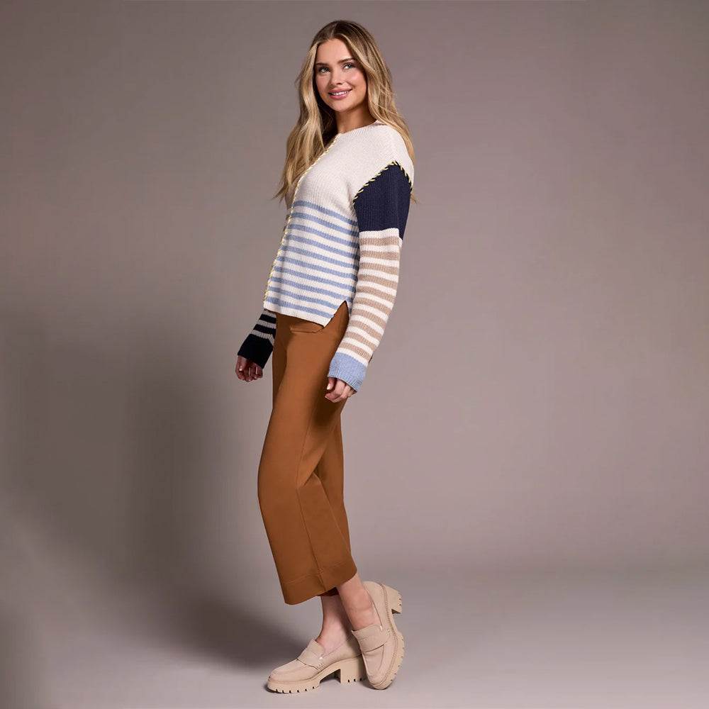 Woman wearing a striped sweater and brown pants against a plain background