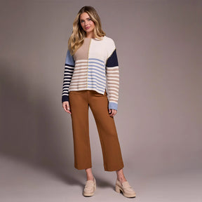 Woman wearing a striped sweater and brown pants against a plain background