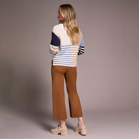 Woman wearing a colorful sweater and brown pants against a plain background