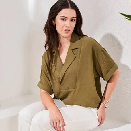 Woman wearing a green blouse and white pants sitting against a light background