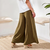 Person wearing olive green wide-leg pants and a white top in a minimal indoor setting.
