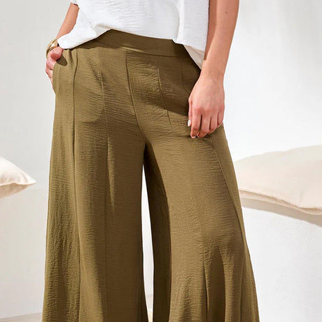 Person wearing olive green wide-leg pants with a white top on a neutral background