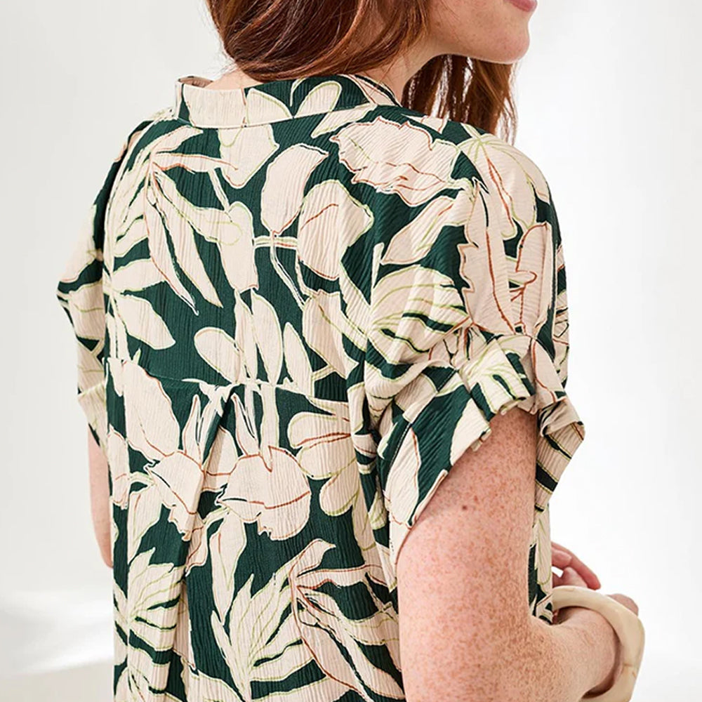 Person wearing a floral patterned shirt with green, white, and beige colors on a plain background