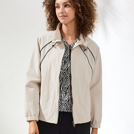 Woman wearing a beige jacket with black accents on a white background