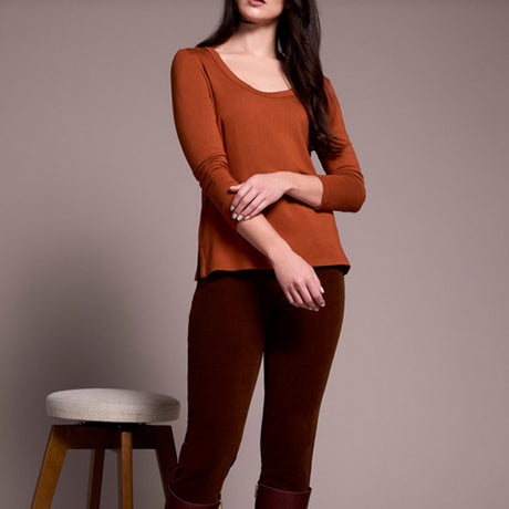 Woman wearing a rust-colored top and pants standing next to a stool against a plain background