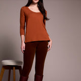 Person wearing a rust-colored long-sleeve top and brown pants against a plain background