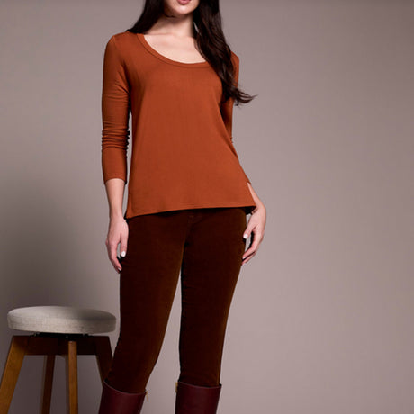 Person wearing a rust-colored long-sleeve top and brown pants against a plain background