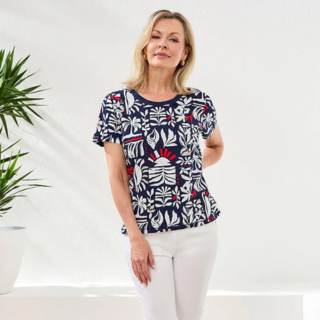 Woman wearing a patterned top with white pants against a white background