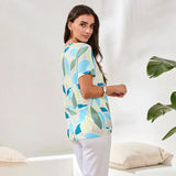 Woman wearing a colorful leaf-patterned shirt in a minimalistic setting with a plant.