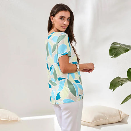 Woman wearing a colorful leaf-patterned shirt in a minimalistic setting with a plant.