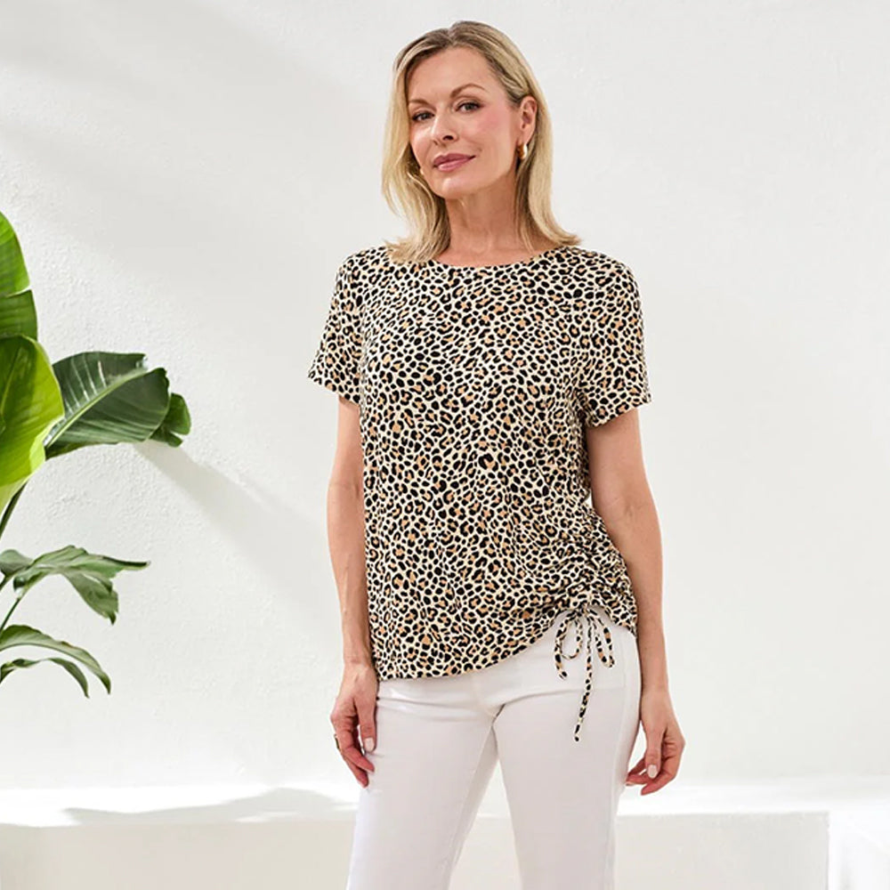 Woman wearing a leopard print top and white pants standing in a minimalistic room with a plant.