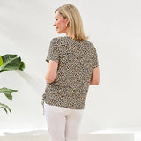 Woman wearing a leopard print top and white pants in a minimal indoor setting