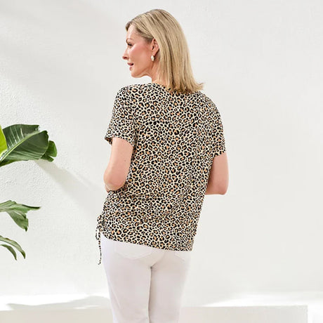 Woman wearing a leopard print top and white pants in a minimal indoor setting