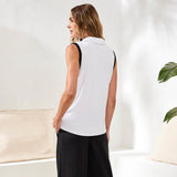 Woman wearing a white sleeveless top and black pants in a minimalistic room.