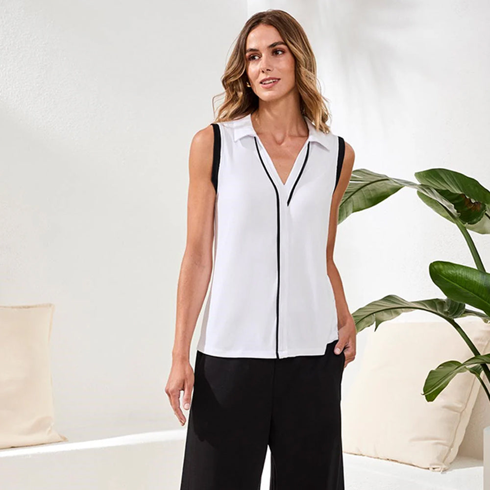 Woman wearing a white sleeveless blouse with black trim in a minimalistic room.