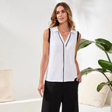 Woman wearing a white sleeveless blouse with black trim in a minimalistic room.