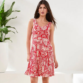Woman wearing a red and white patterned dress standing next to a plant on a white background