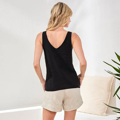 Woman wearing a black tank top and beige shorts against a white background