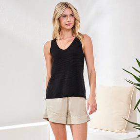 Woman wearing a black tank top and beige shorts against a white background