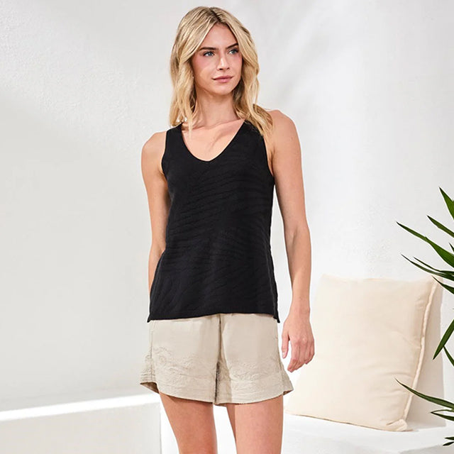 Woman wearing a black tank top and beige shorts against a white background