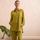 Woman wearing a green button shirt with her hands in her pockets.