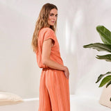 Woman wearing an orange jumpsuit standing in a minimalistic room with a plant.