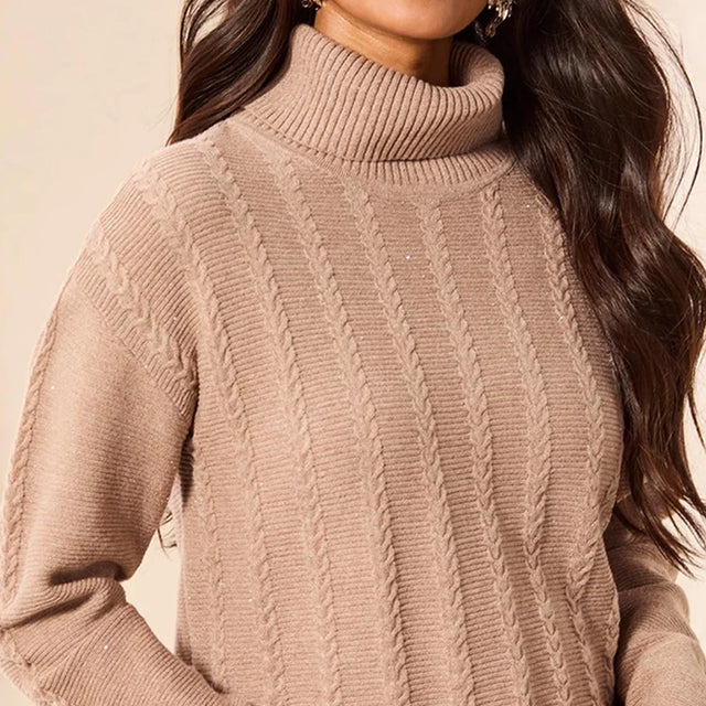 A close-up of a woman wearing a ribbed turtleneck sweater in a warm taupe-beige color with vertical cable knit details.