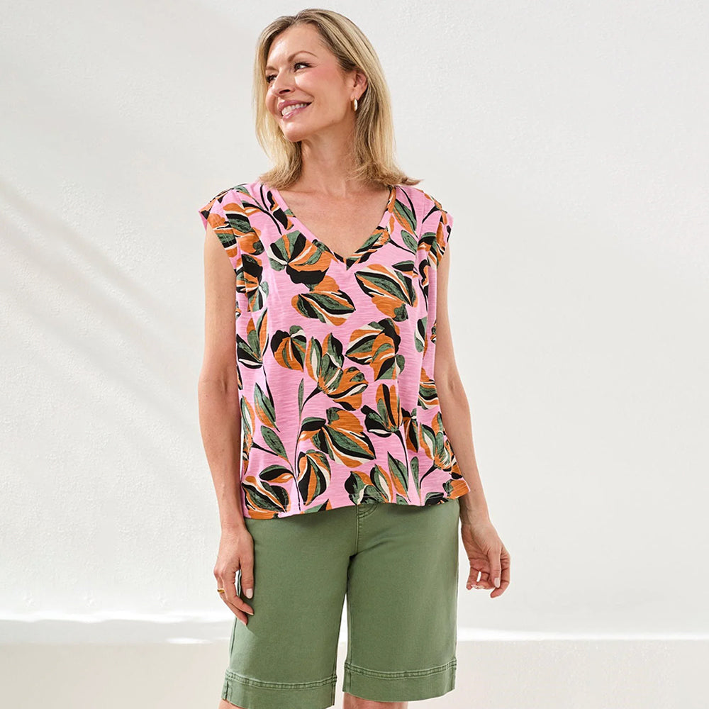 Woman wearing a pink top with leaf pattern and green shorts on a white background