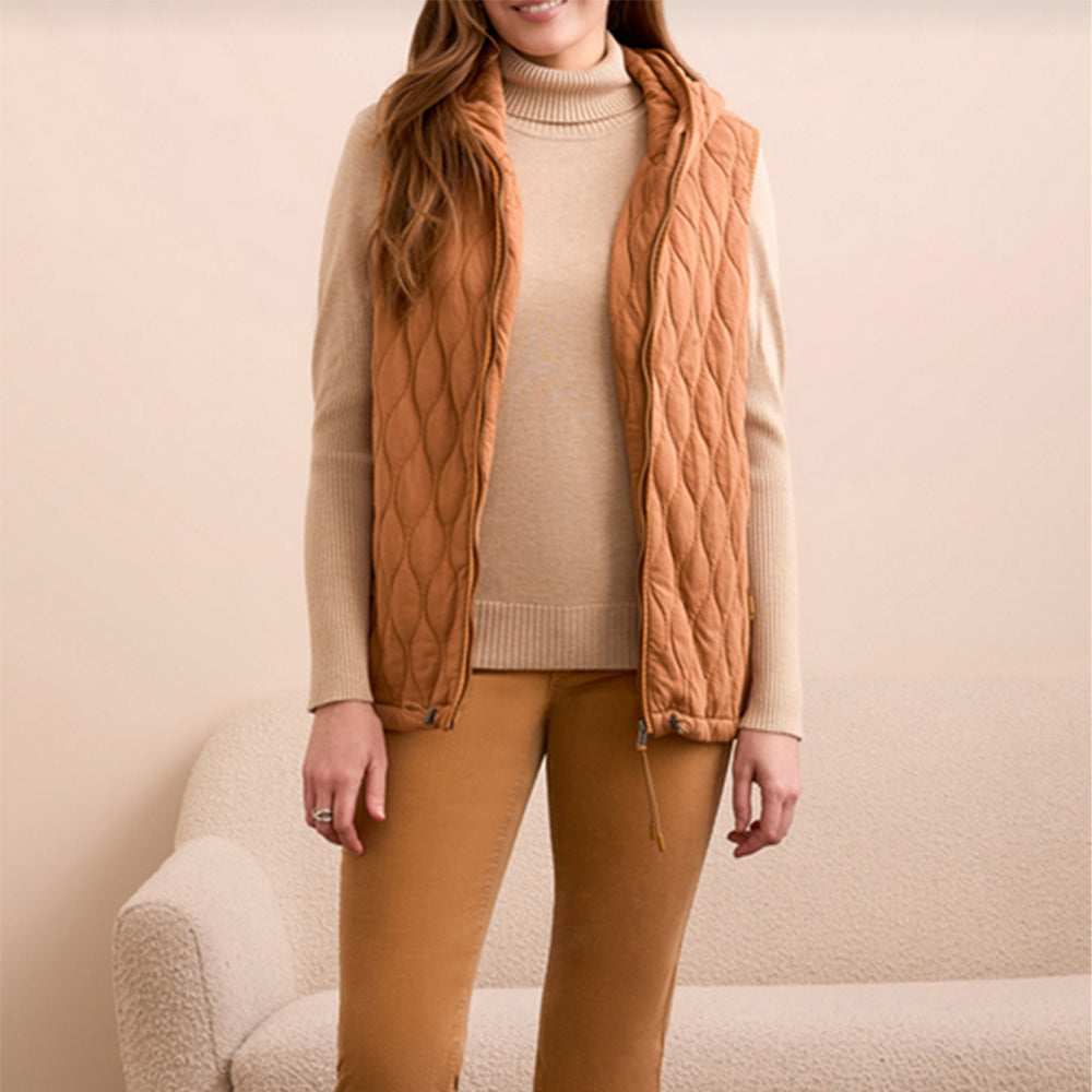 Woman wearing a wheat colored vest over a cream colored sweater with wheat colored pants.