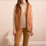 Woman wearing a wheat colored vest over a cream colored sweater with wheat colored pants.