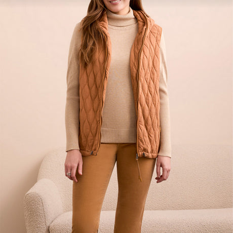 Woman wearing a wheat colored vest over a cream colored sweater with wheat colored pants.