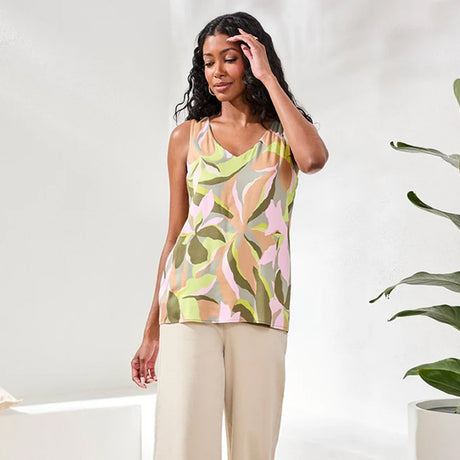 Woman wearing a patterned top and beige pants against a white background