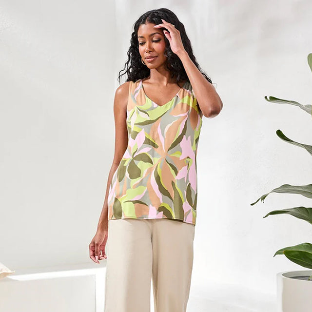 Woman wearing a patterned top and beige pants against a white background