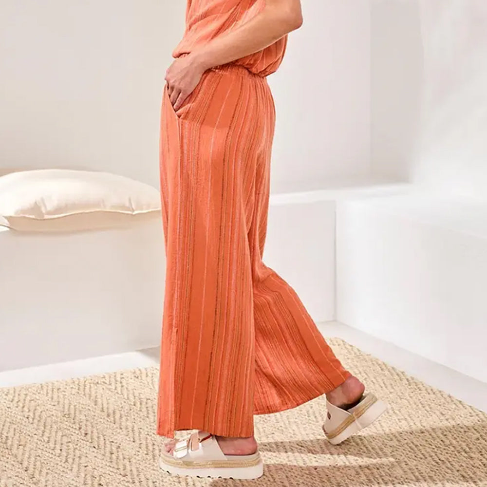Person wearing an orange outfit with wide-leg pants and sandals on a neutral background