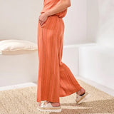 Person wearing an orange outfit with wide-leg pants and sandals on a neutral background