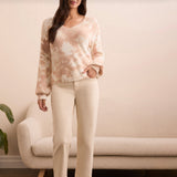 Woman wearing a tie-dye sweater and white pants standing in a room with a beige couch and plant.