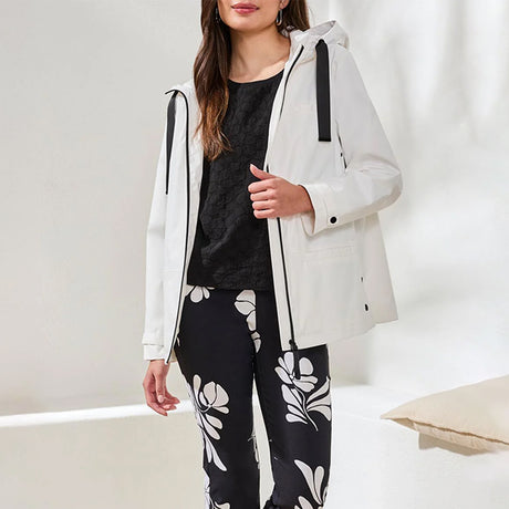 Woman wearing a white coat over a black top and floral pants in a minimal indoor setting.