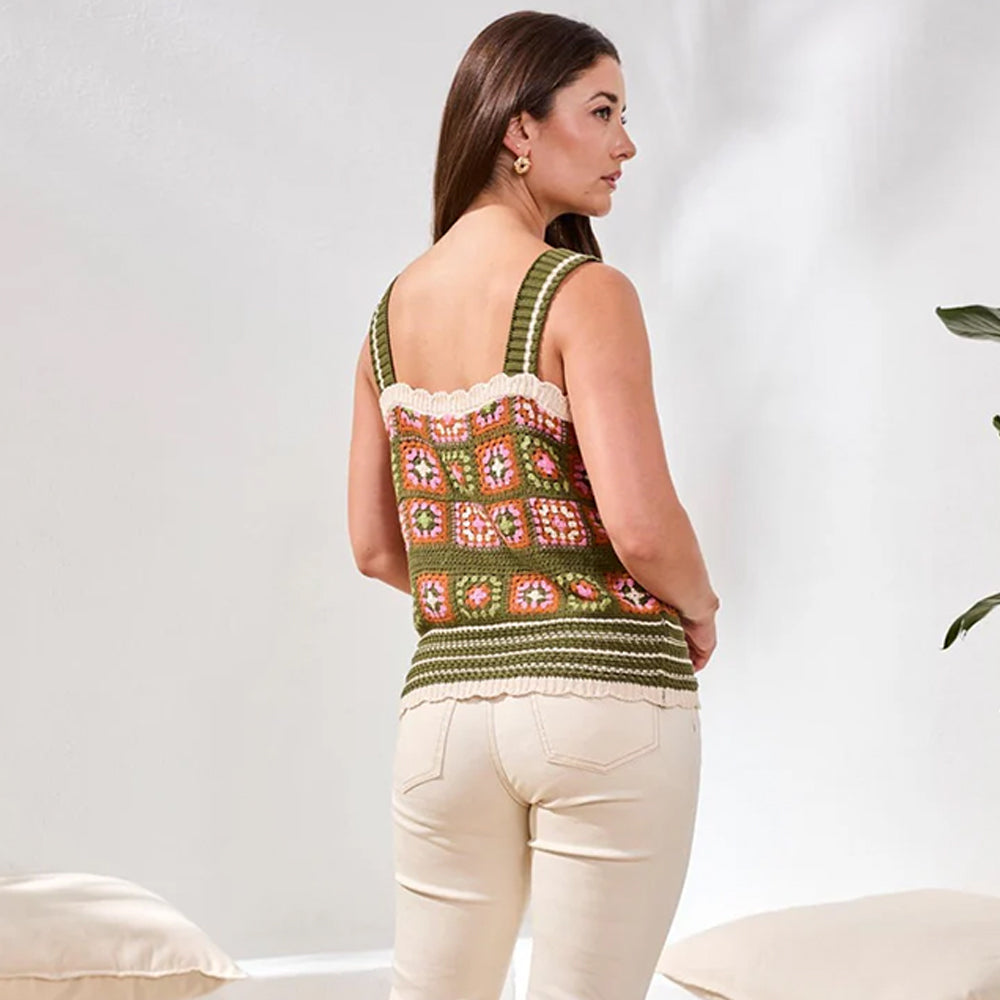 Woman wearing a patterned tank top and white pants against a plain background