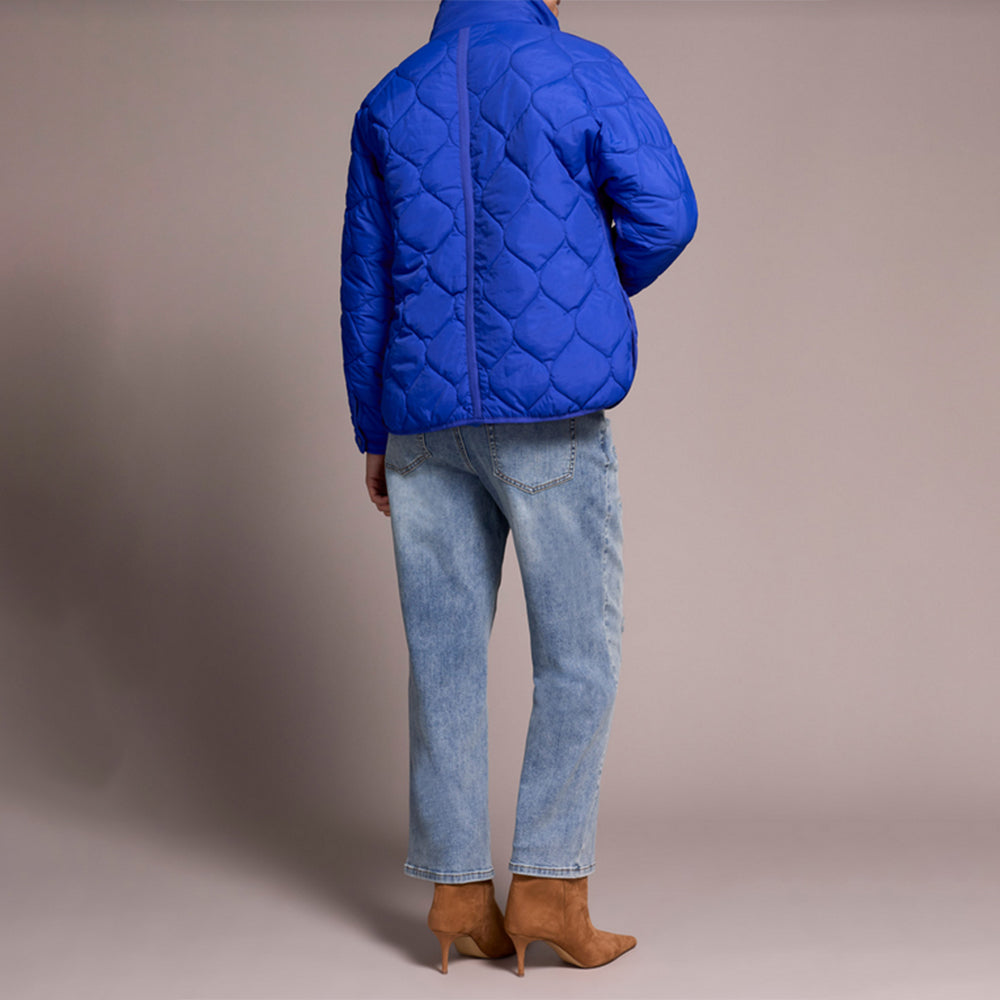 Person wearing a blue quilted jacket, light blue jeans, and brown boots on a beige background