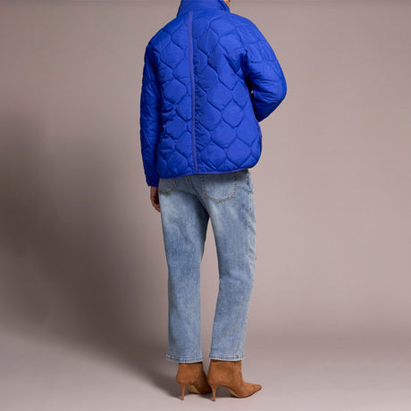 Person wearing a blue quilted jacket, light blue jeans, and brown boots on a beige background