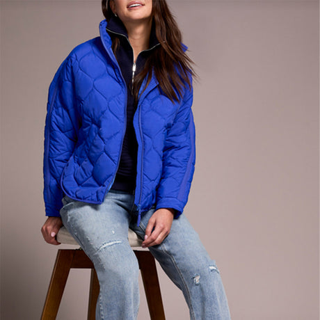 Lady wearing blue puffer jacket with jeans, sitting on a stool.