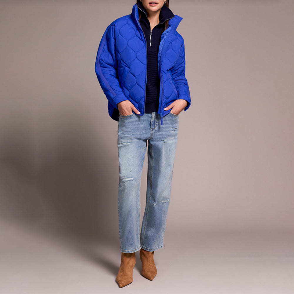 Person wearing a blue quilted jacket, jeans, and brown boots on a plain background