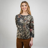 Woman wearing a patterned long-sleeve top and brown pants against a white background