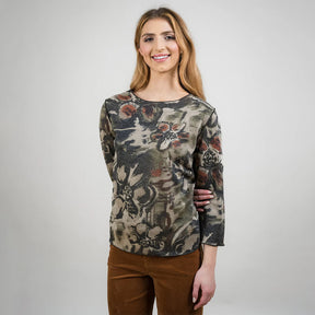Woman wearing a patterned long-sleeve top and brown pants against a white background