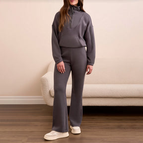 Person wearing a gray tracksuit standing in a room with a beige couch.