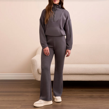 Person wearing a gray tracksuit standing in a room with a beige couch.