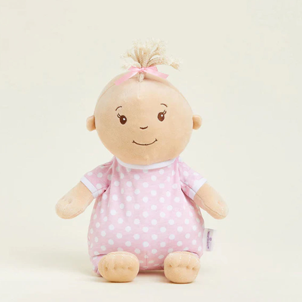 Stuffed toy baby doll with pink polka dot outfit on a light beige background