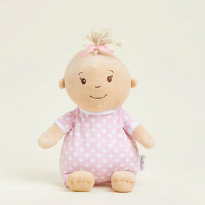 Stuffed toy baby doll with pink polka dot outfit on a light beige background
