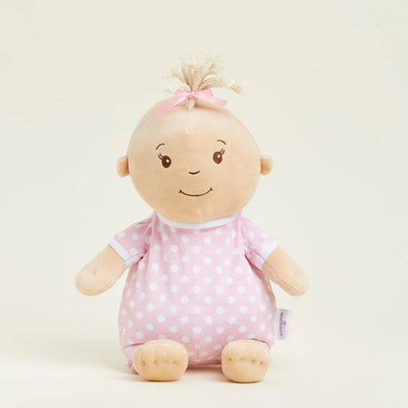 Stuffed toy baby doll with pink polka dot outfit on a light beige background